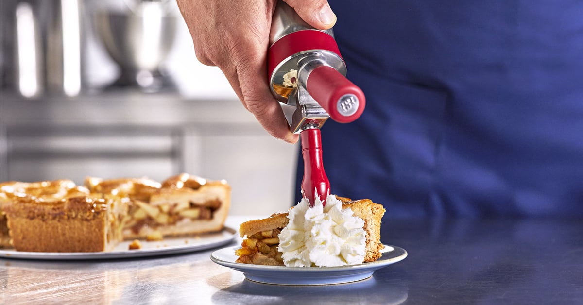 Hand spuit slagroom op een stuk taart in een professionele keuken