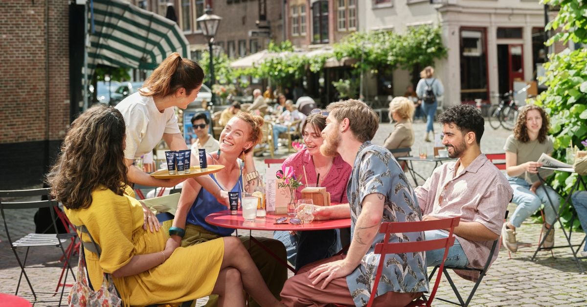 Gasten genieten op een zonnig terras terwijl de serveerster hen zonnebrandcrème aanbiedt