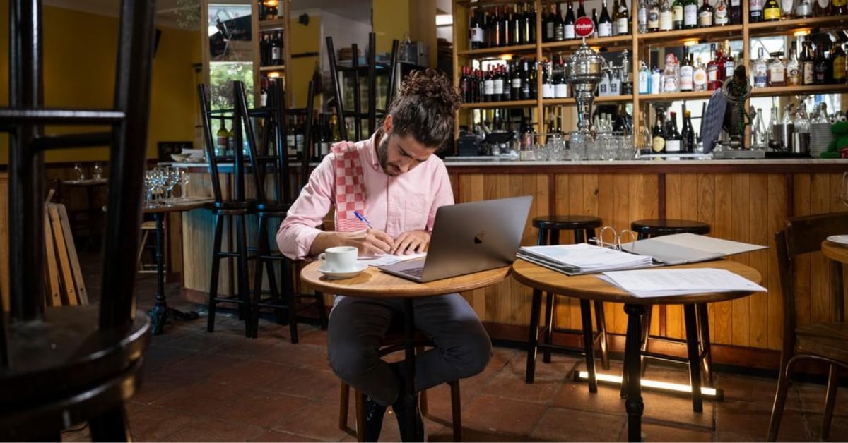 Ondernemer werkt met laptop en papieren aan tafel in een horecazaak