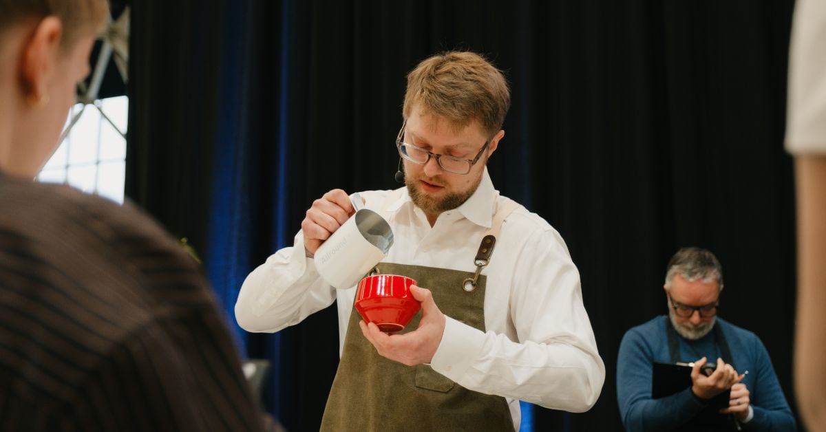 Bram Dekker maakt latte art tijdens latte art kampioenschap met jury op de achtergrond