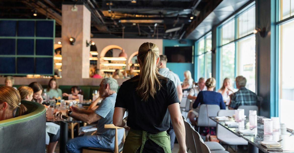 Horecamedewerker loopt door een drukbezocht restaurant tijdens de service