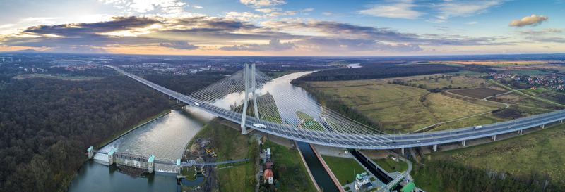 Panoramic aerial view of a cable-stayed bridge and river corridor with highway traffic across a wide landscape.