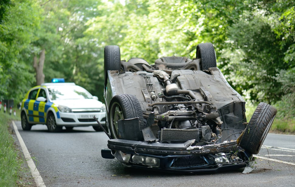 Overturned car on a rural road with a police vehicle in the background