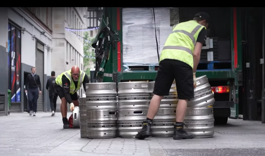 Delivery workers unloading kegs from a truck onto a city street curb