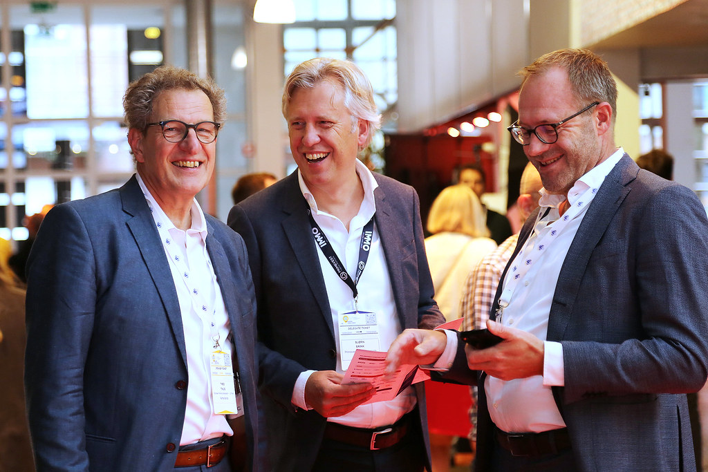 Three business professionals networking at a mobility conference, smiling and reviewing documents