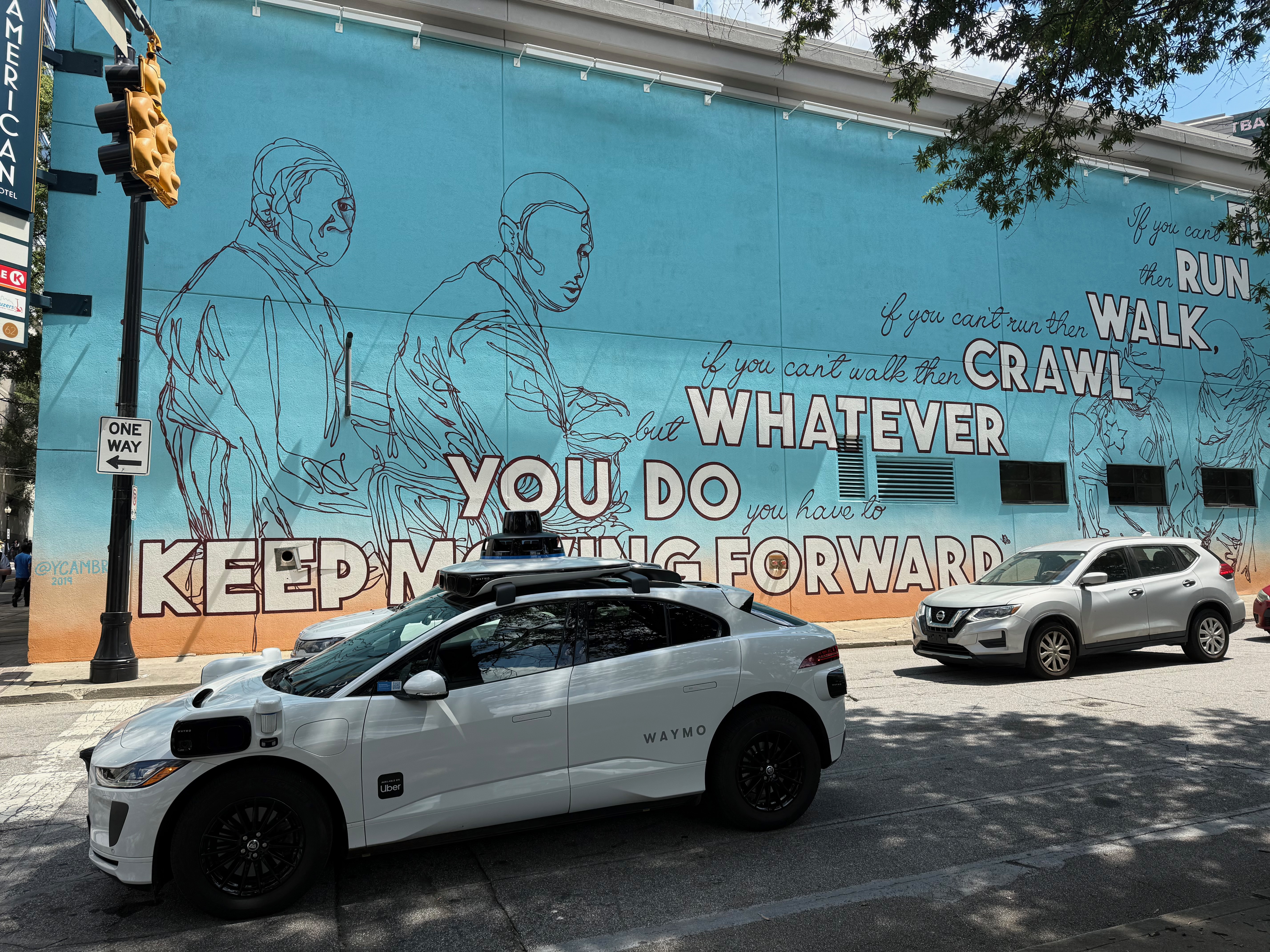 Waymo autonomous car driving in Atlanta near mural with text Keep Moving Forward