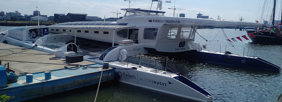 Three boats moored alongside a marina dock, with harbour facilities and calm waters in the background.