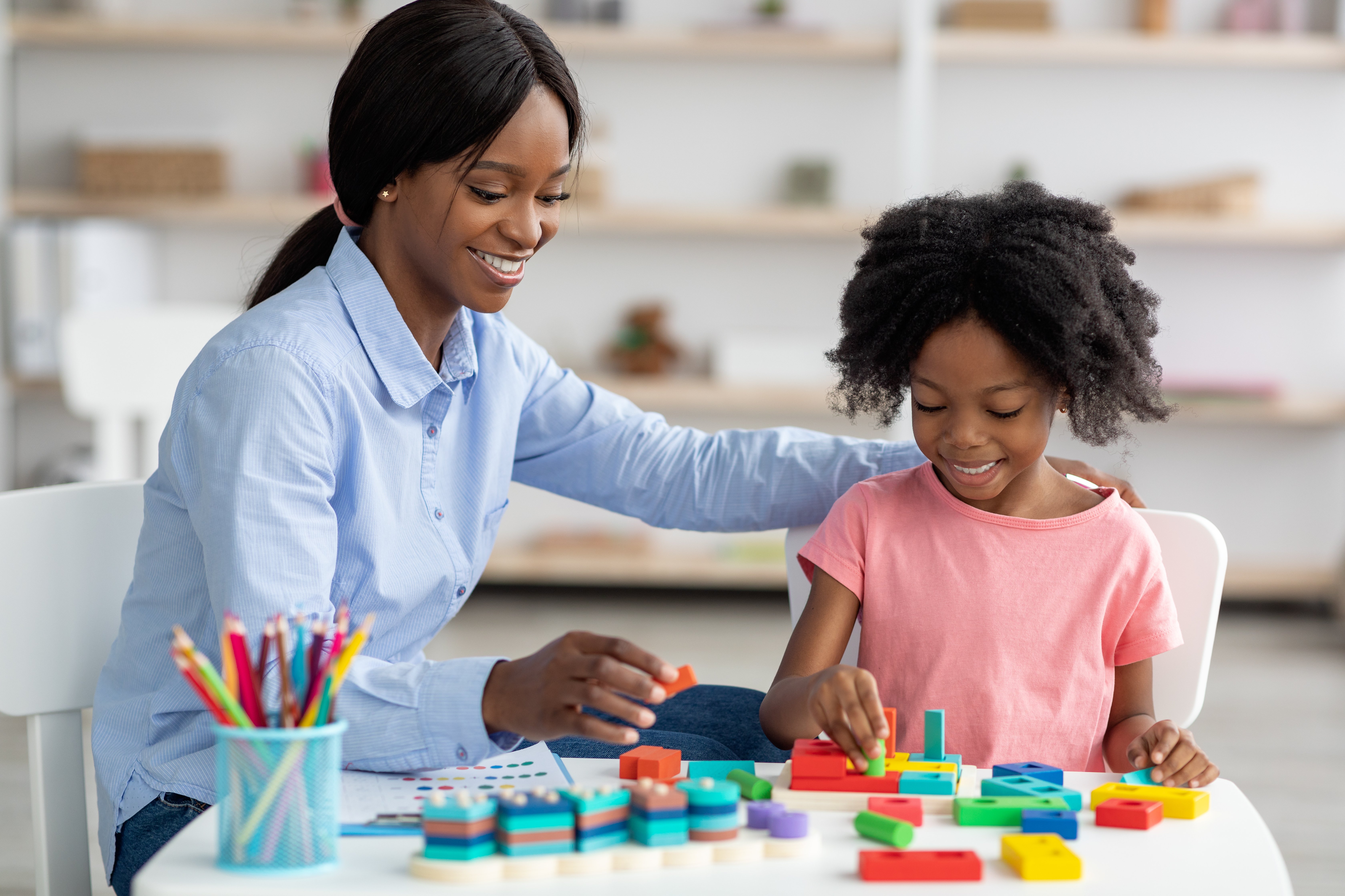 A woman interacting with a young girl at a table doing an activity