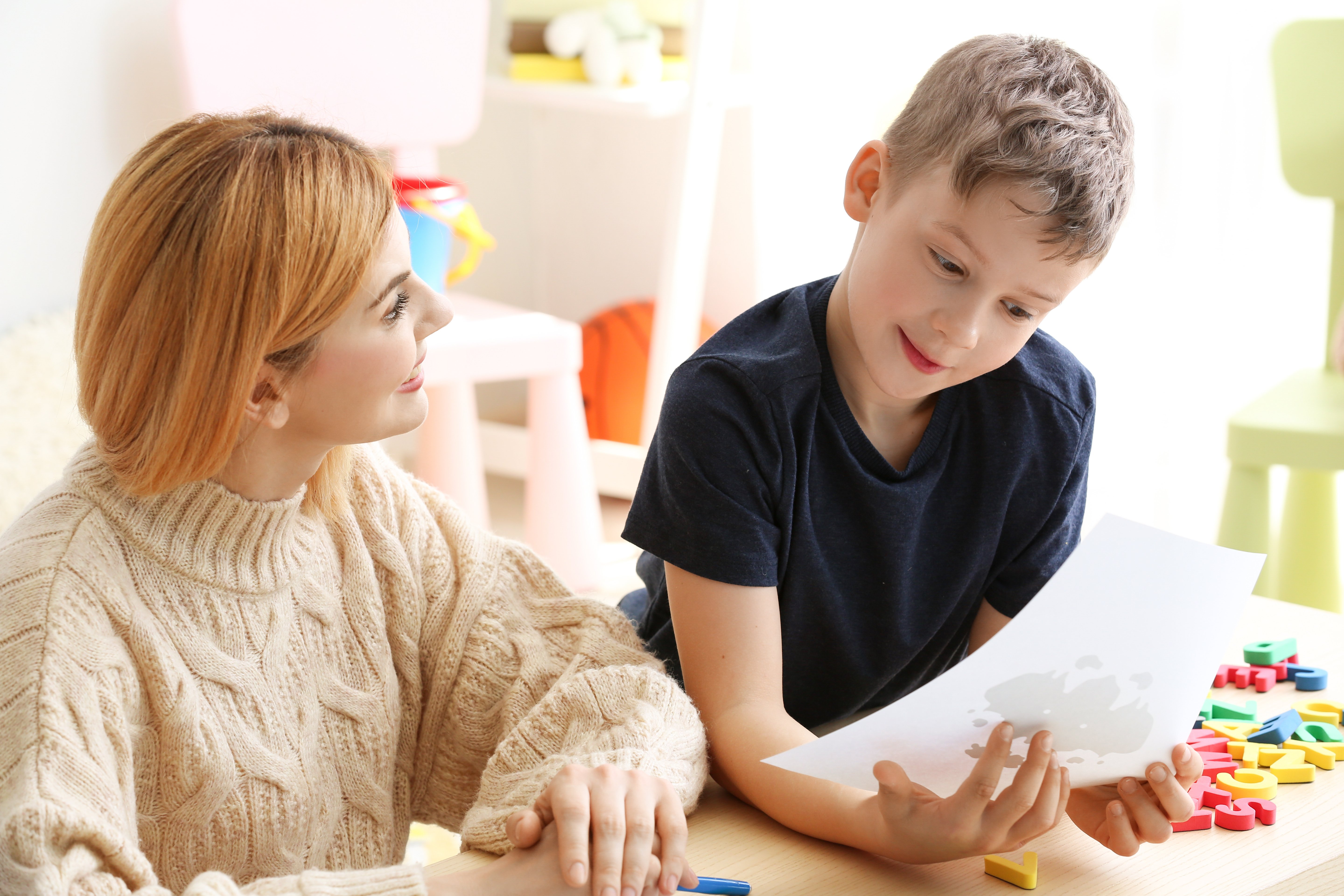A young male child looking at a piece of paper an adult looking at him