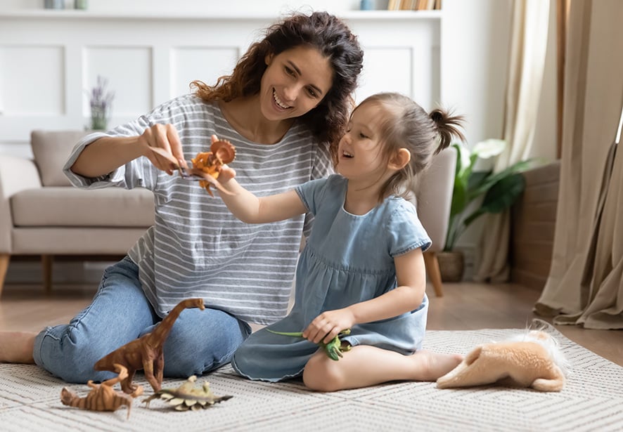 A woman playing with her daughter sitting on the floor together with toys