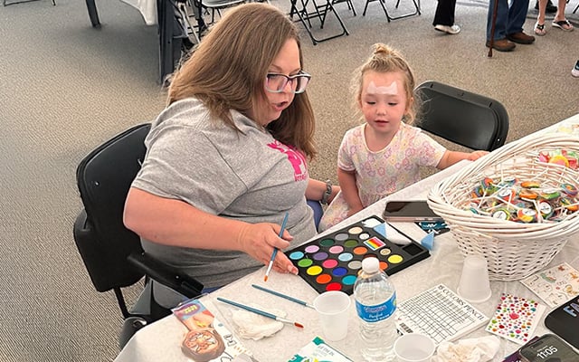 A Reid Health team member helping a young girl pick out paint for face painting.