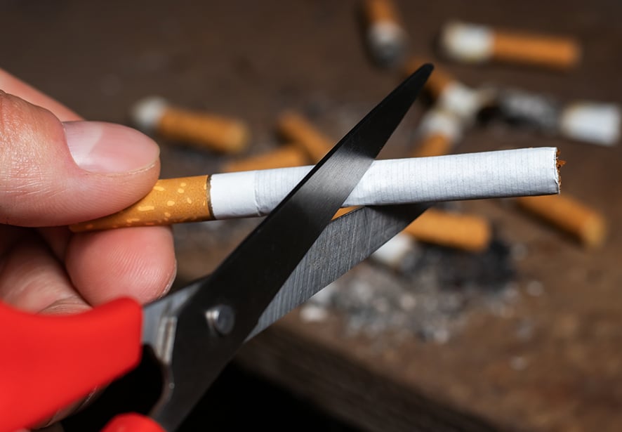 A person cutting up their cigarette with a pair of scissors 