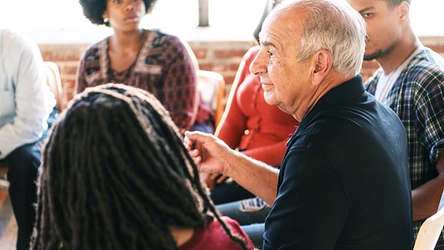 A diverse group of people in a discussion circle, with an older man talking