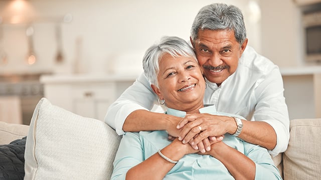 A husband leaning over a couch hugging his wfie
