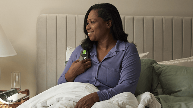 A women in bed smiling while using the Inspire remote 