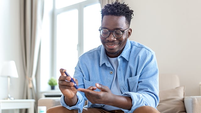 African man is sitting at the sofa at the home and taking blood from his finger