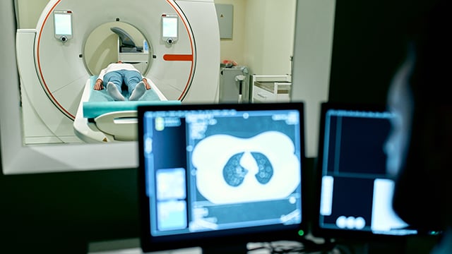 An imaging tech observing a screen while a patient is having a CT scan