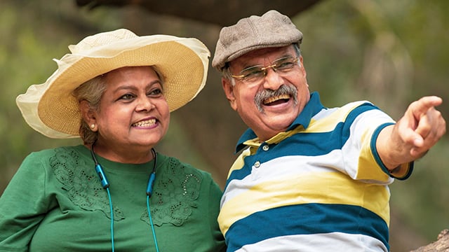 A husband and wife wearing hats looking to the right with the man pointing 