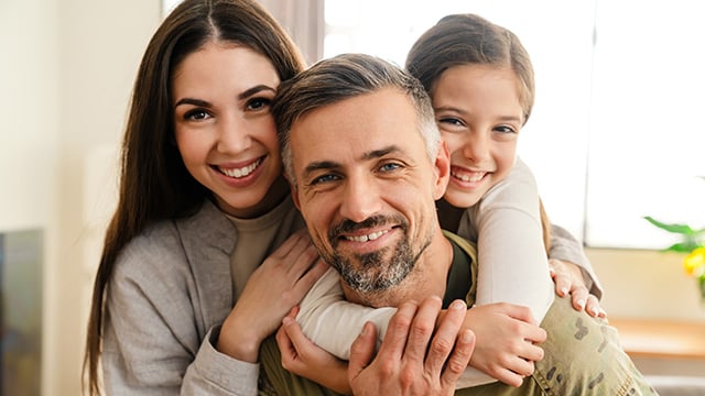 A man smiling with his daughters embracing him smiling