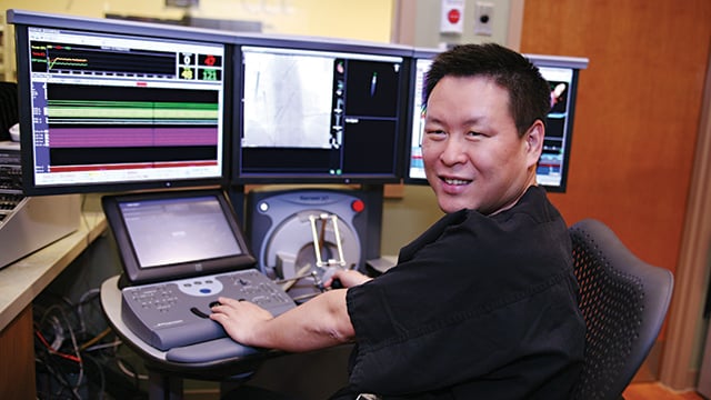 Dr. Han, Reid Health Cardiologist smiling in front of heart monitoring equipment