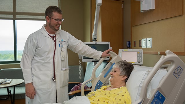 Reid Health Cardiologist, Dr. John McGinty smiling at a patient in her hospital bed