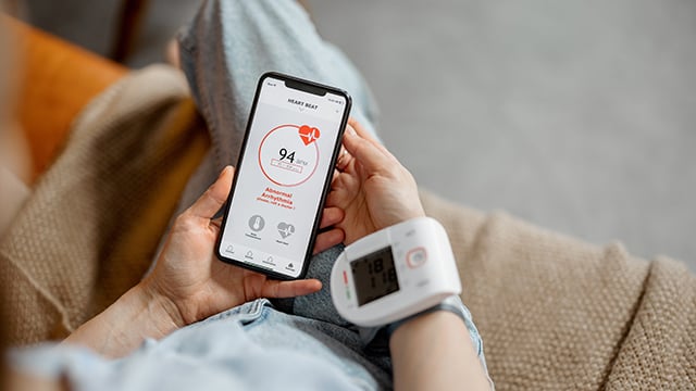 A woman monitoring her blood pressure with the result showing on her phone