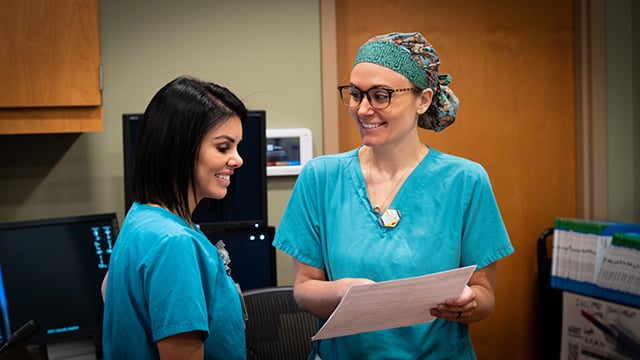 Two nurses in the cardiac cath lab smiling and reviewing information together