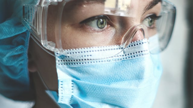 A women in surgical mask, cap and eye goggles. 