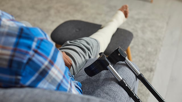 photo of crutches in the background of a man's leg in cast on the sofa