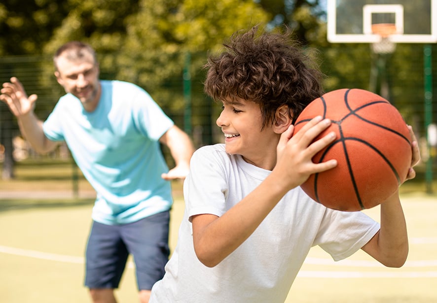 A close up image of teenage boy trying to keep the basketball away from his dad