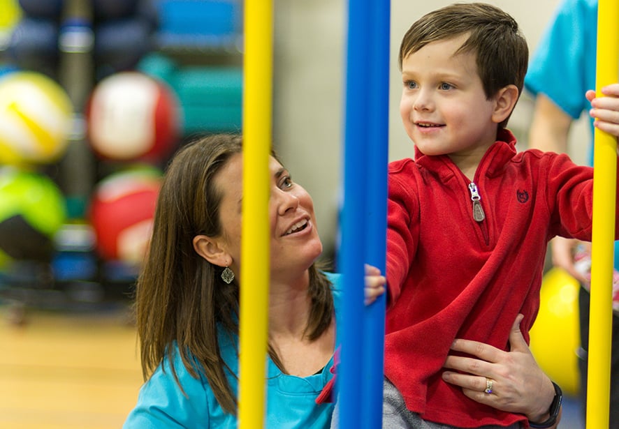 A young boy playing on therapy equipment with help from his physical therapist 