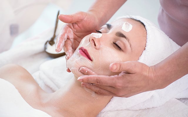 A women laying down with a spa employee performing a facial service. 