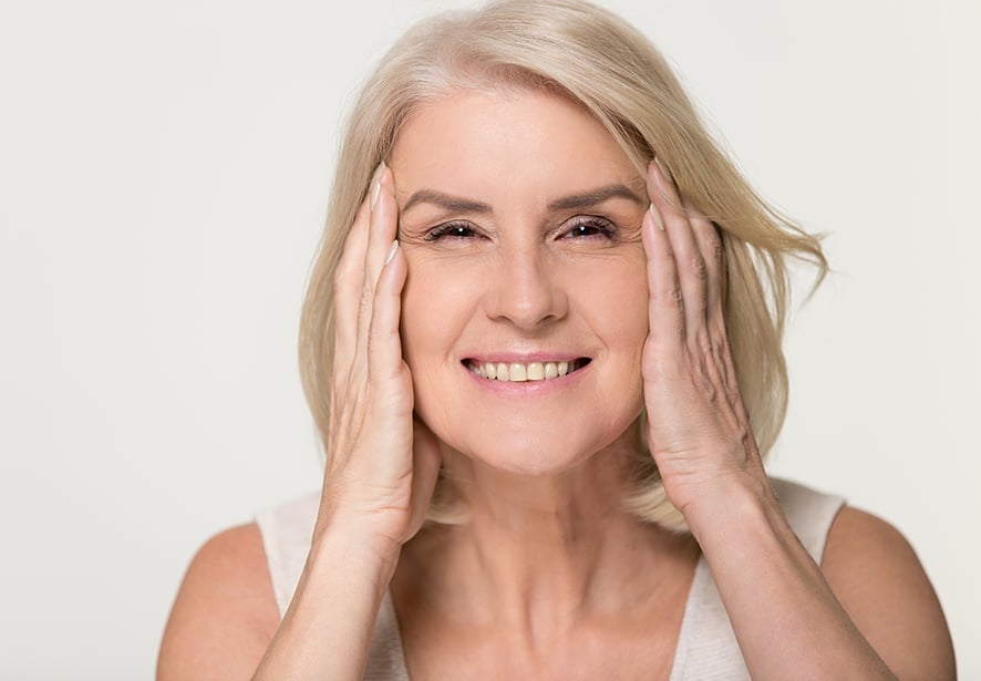 An older woman smiling with her hands framing her face