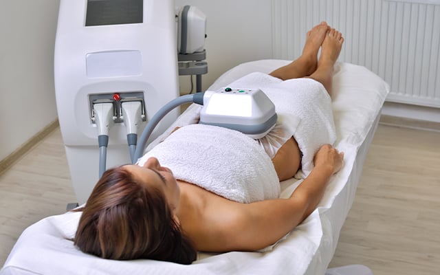 A woman laying on a spa table receiving a CoolSculpting treatment.