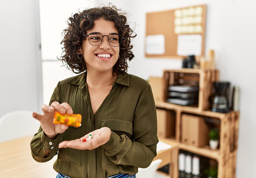 A women smiling while putting medications into her hand from a medication bottle.