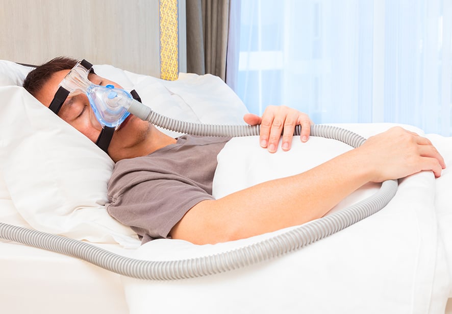 A man wearing CPAP mask, sleeping on his bed