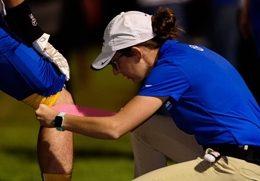 Reid Athletic Trainer, Hannah Gross taping a knee during a local high school football game