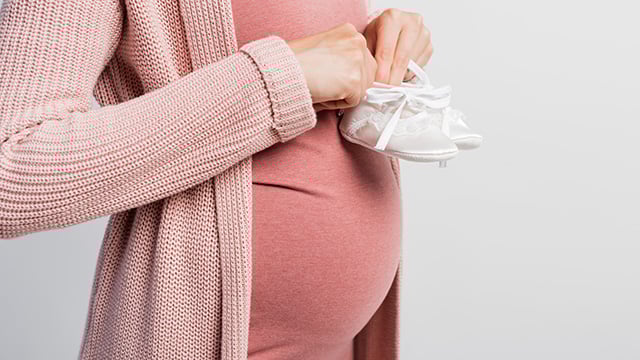 A pregnant woman holding a pair of baby shoes over her belly 