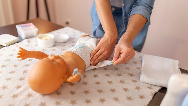 A women learning to change a newborn baby diaper on a doll
