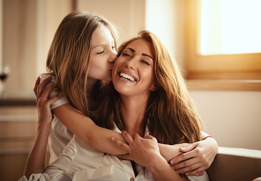 A woman smiling with her daughter kissing her cheek