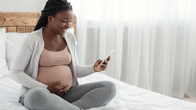 A young soon to be mom sitting on her bed looking at her phone
