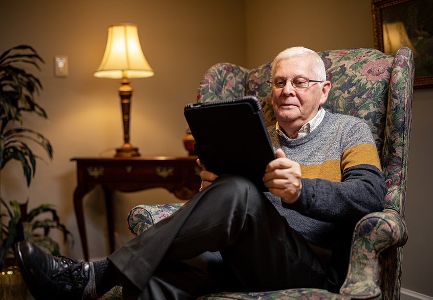 An older gentleman sitting in his card looking at his tablet