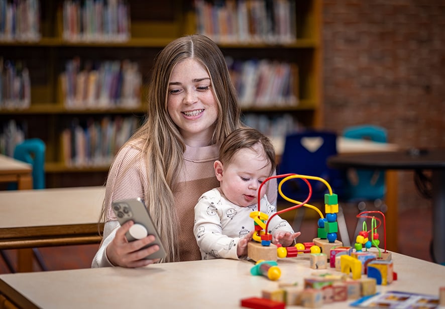 A mom holding her baby, looking at her phone