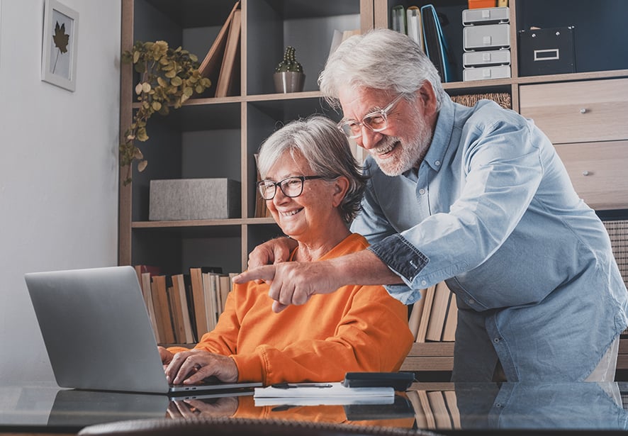 An older man and woman looking a computer together with the man pointing at the screen