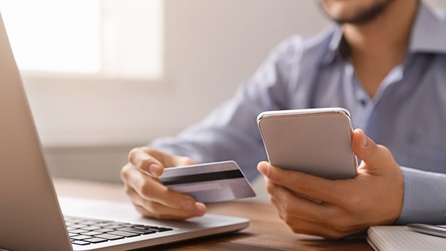 A close up view of a man holding his phone in one hand and a credit card in another