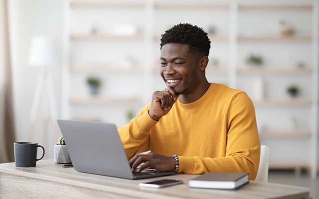 A young black male smiling while working on a computer