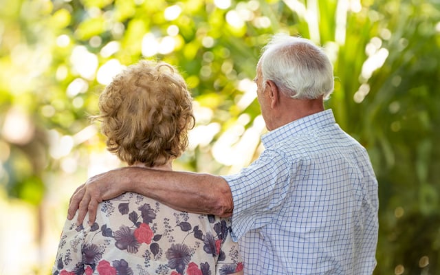 A older couple with backs to the camera with the man's arm on the woman's shoulder