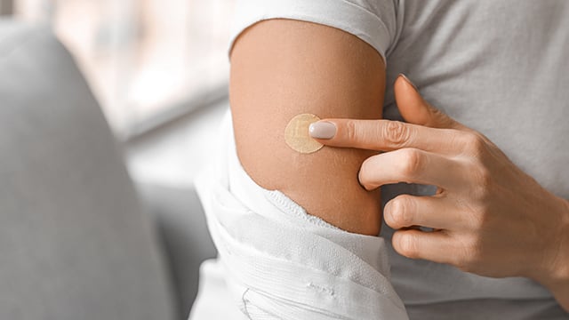 A woman applying a nicotine patch to her arm 