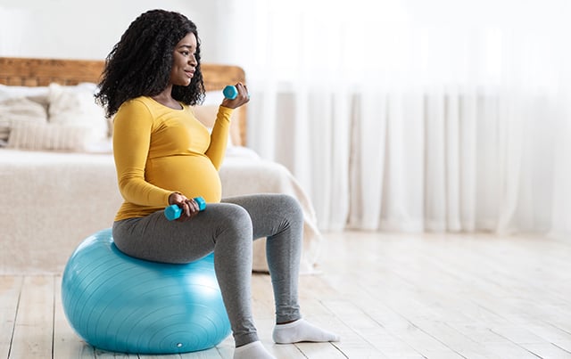 A pregnant woman sitting on an exercise ball and lifting weights 