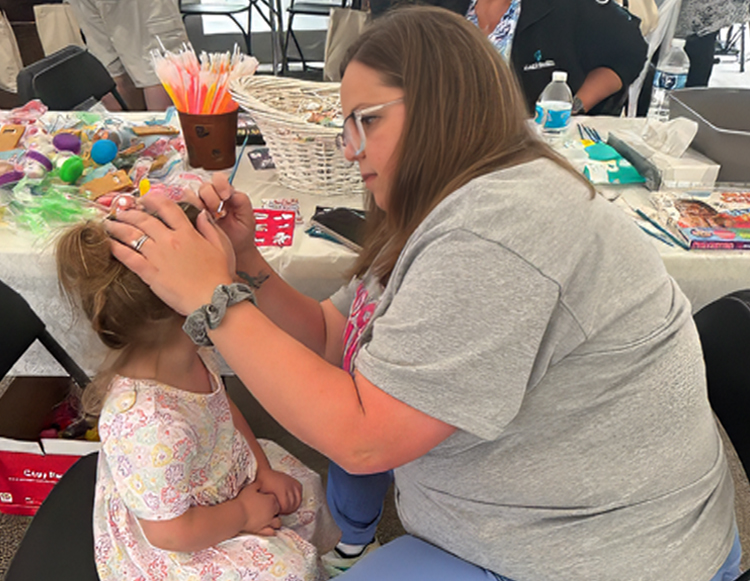 A Reid Health team member painting the face of a young girl at the 2025 Cancer Survivors Day